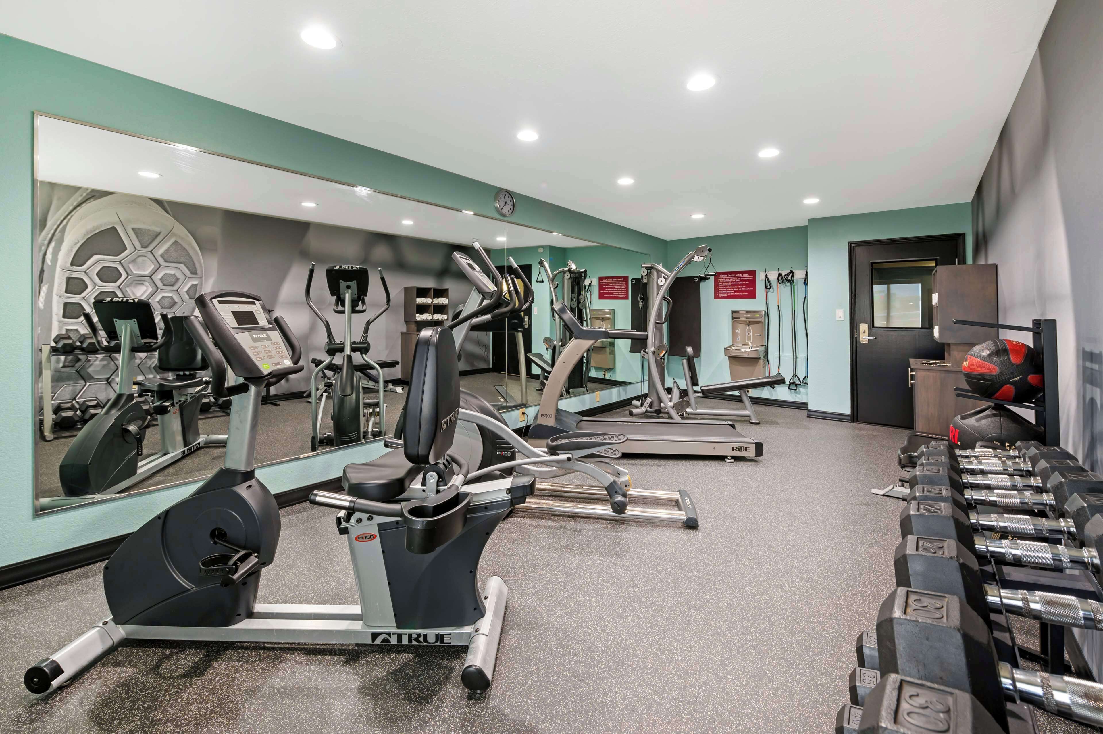Et fitnesscenter med forskellig træningsudstyr, herunder løbebånd, crosstrainere og vægte.