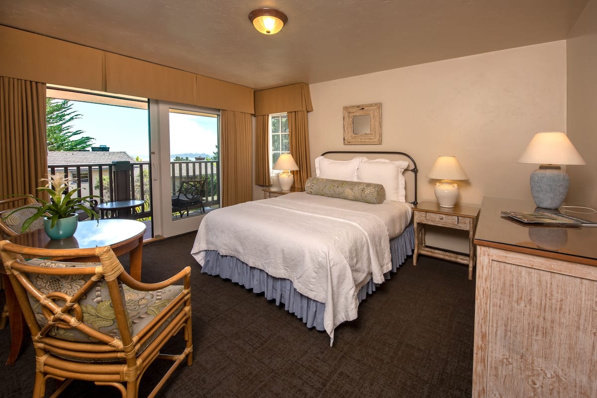 A hotel room with a bed, a chair, a table, and a balcony.