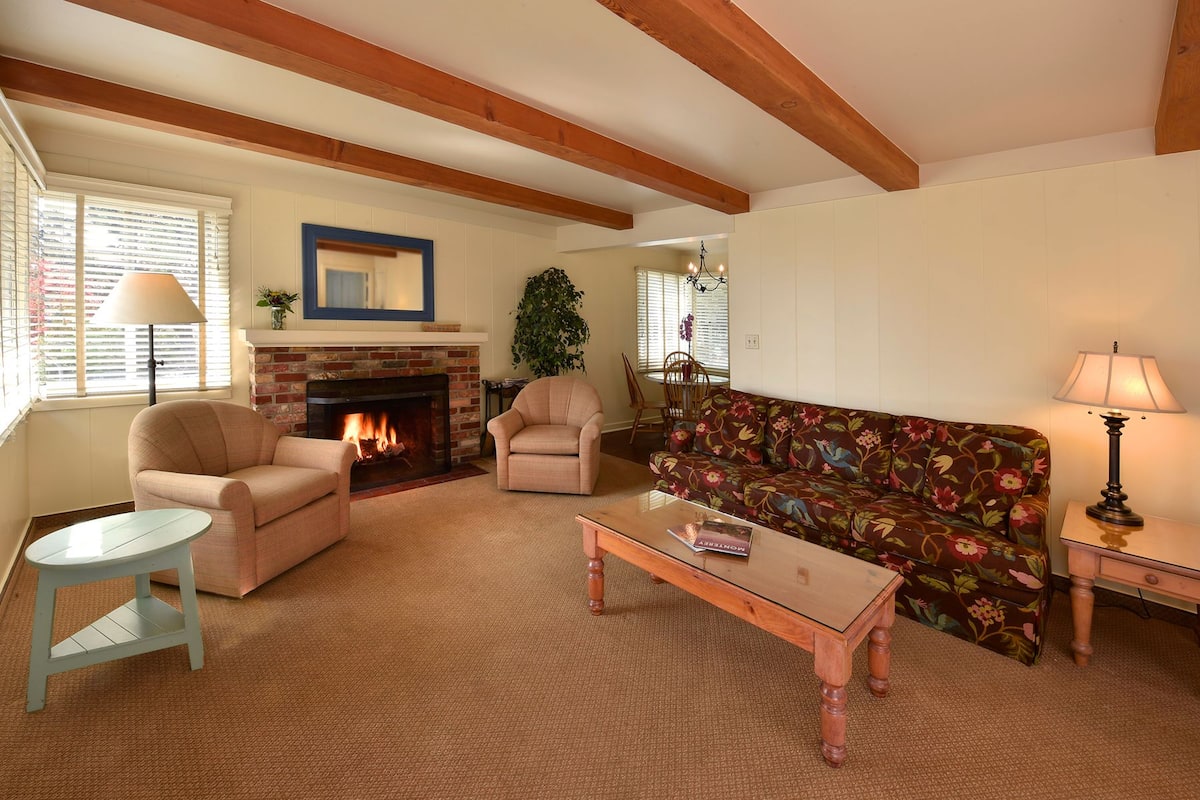 A living room with a fireplace, two armchairs, a sofa, a coffee table, and a lamp.