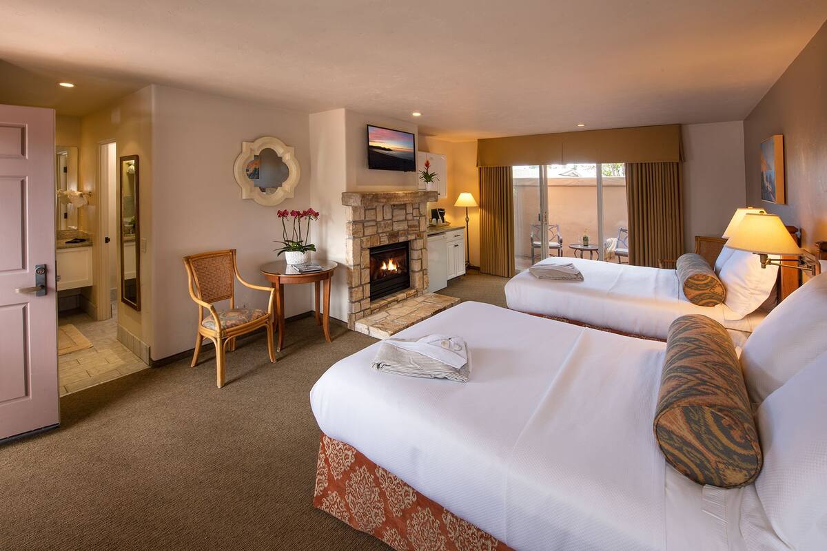 A hotel room with two beds, a fireplace, a TV, and a balcony with curtains.
