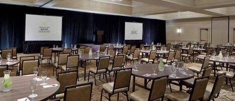 Une grande salle de conférence dotée de nombreuses tables et chaises, d’une scène avec un écran et d’un sol recouvert de moquette.