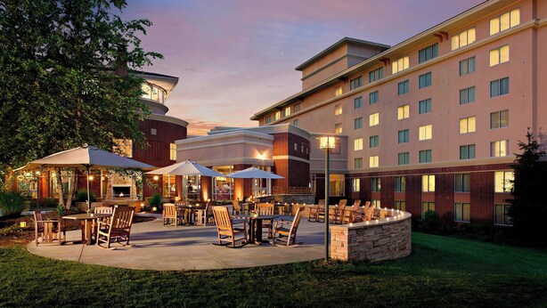 A hotel courtyard with outdoor seating, a stone fire pit, and a large building with multiple windows.