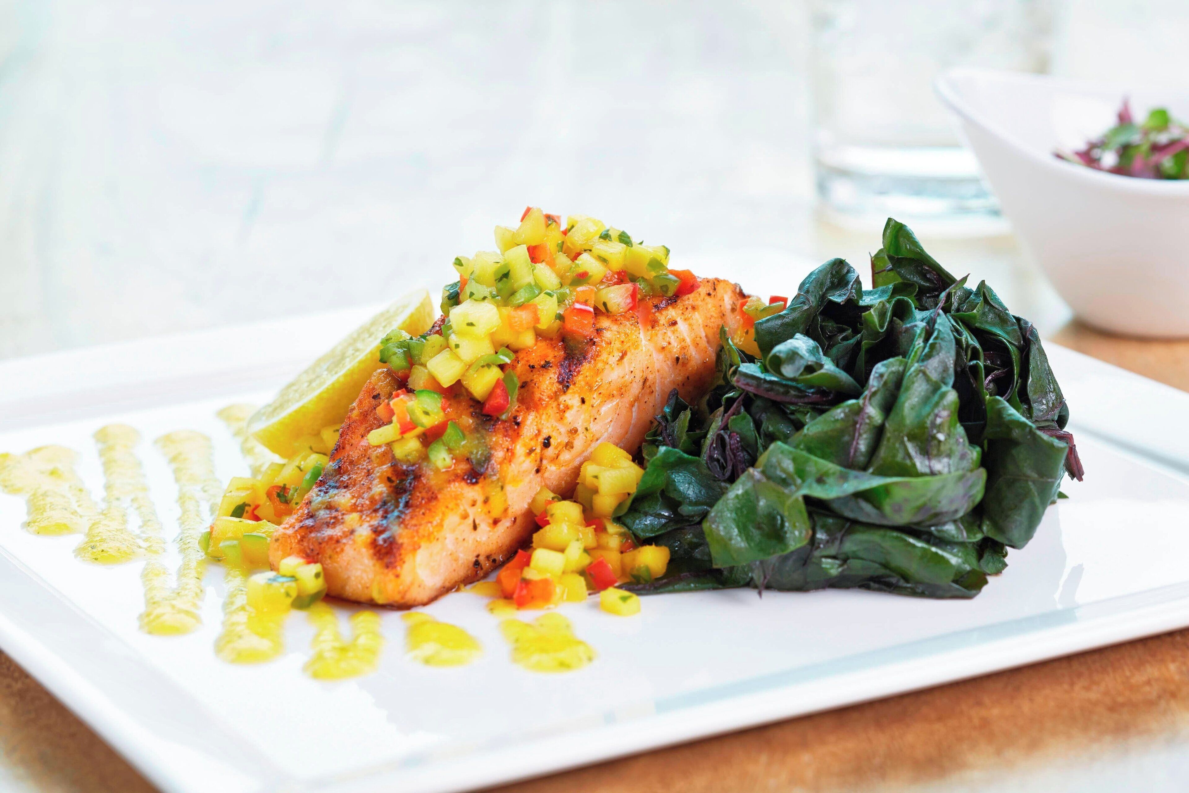 A plate with grilled salmon, a side of spinach, and a mango salsa.