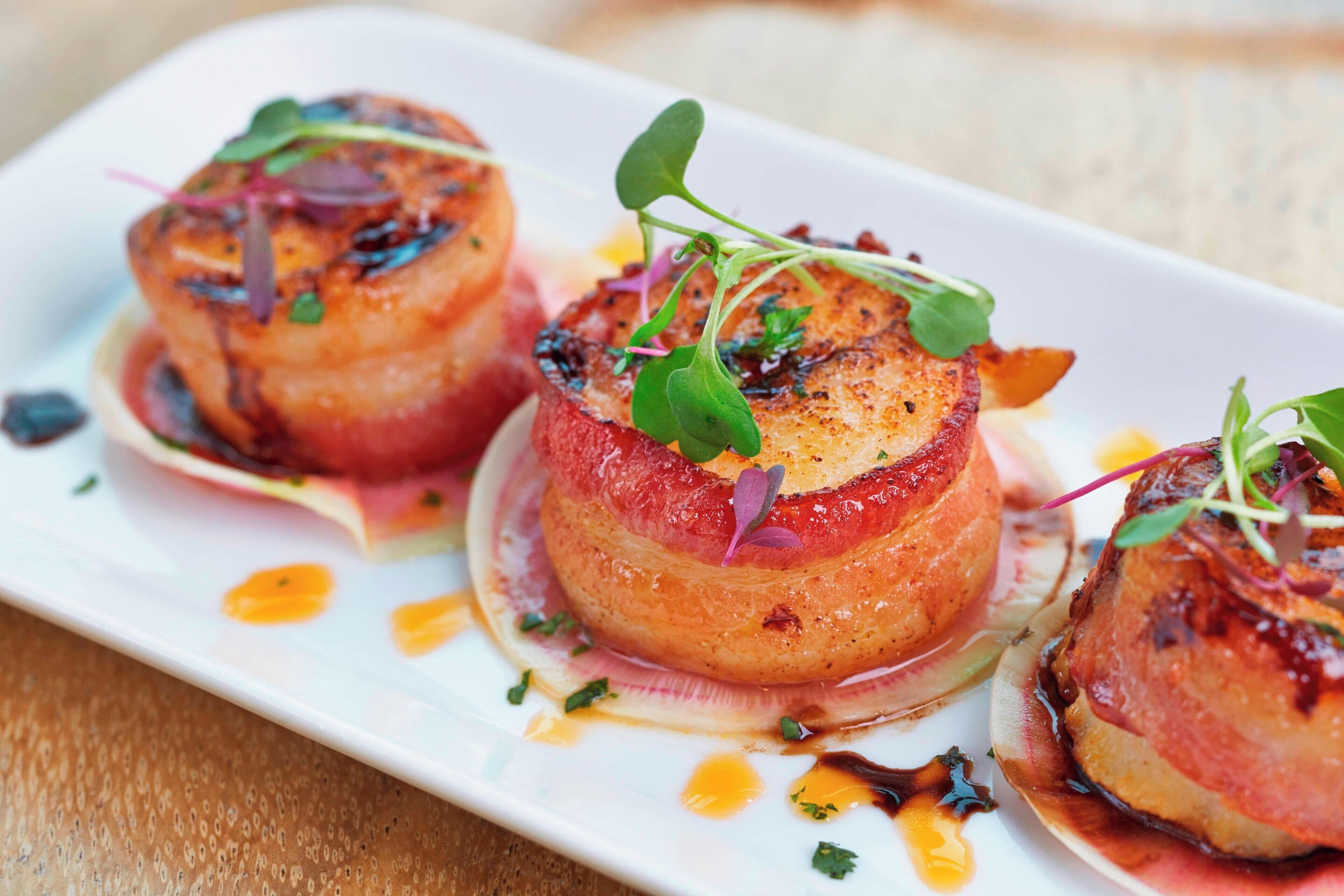 Three scallops on a white plate with a sauce and garnish.