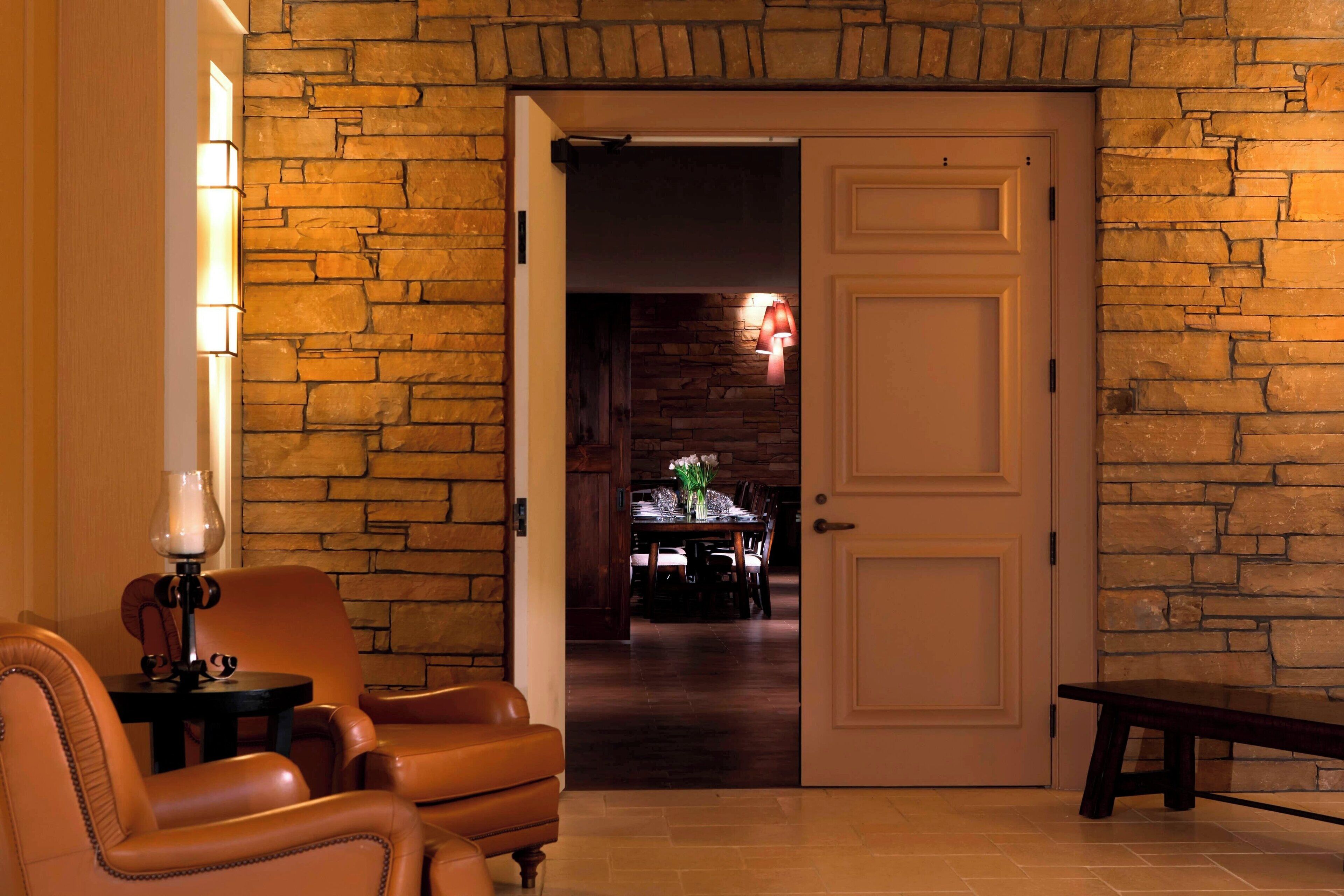 A room with a stone wall, a white door, a dining table with chairs, and a bench.