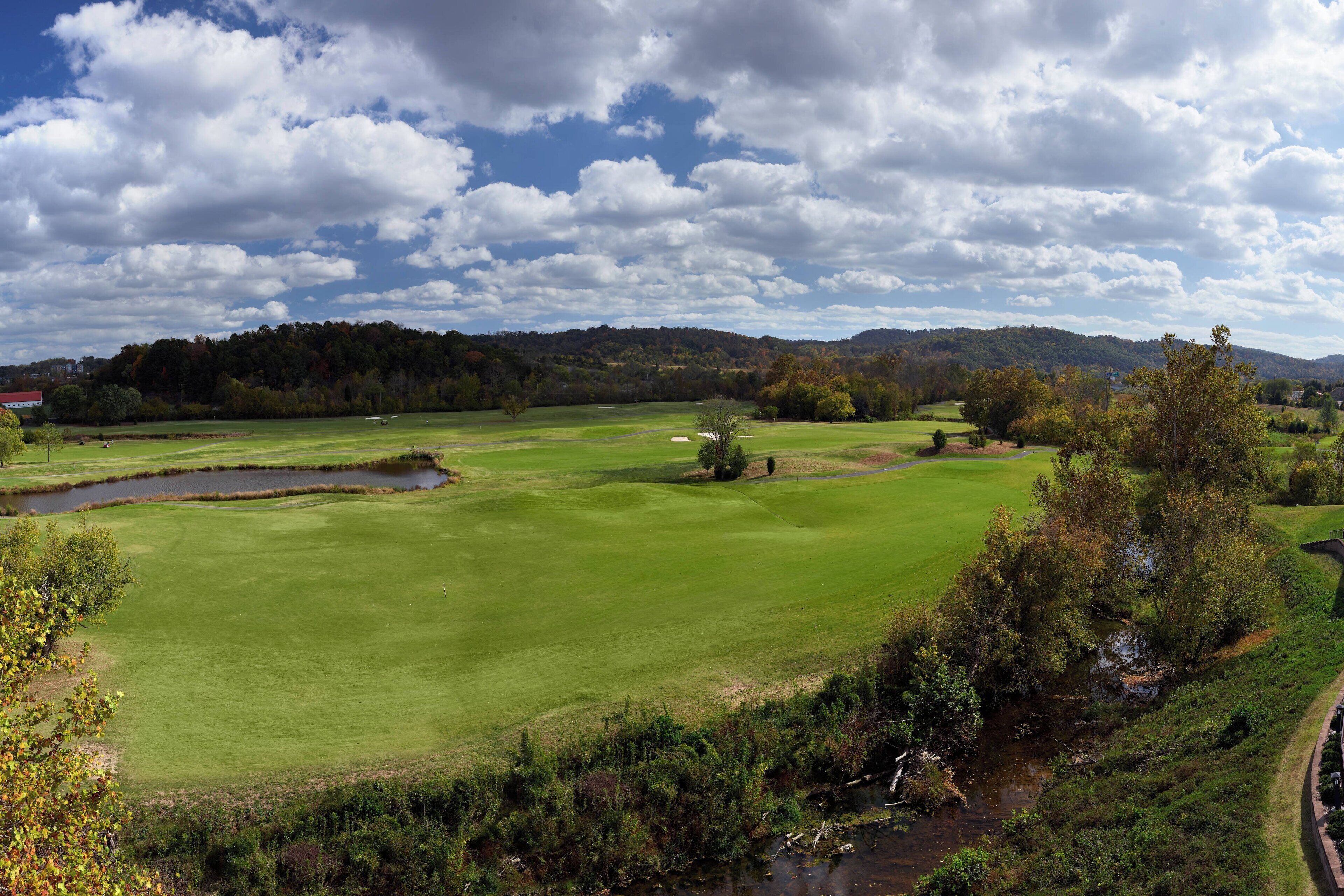 Un parcours de golf avec un étang, des arbres et une colline qui se dessine à l’horizon.