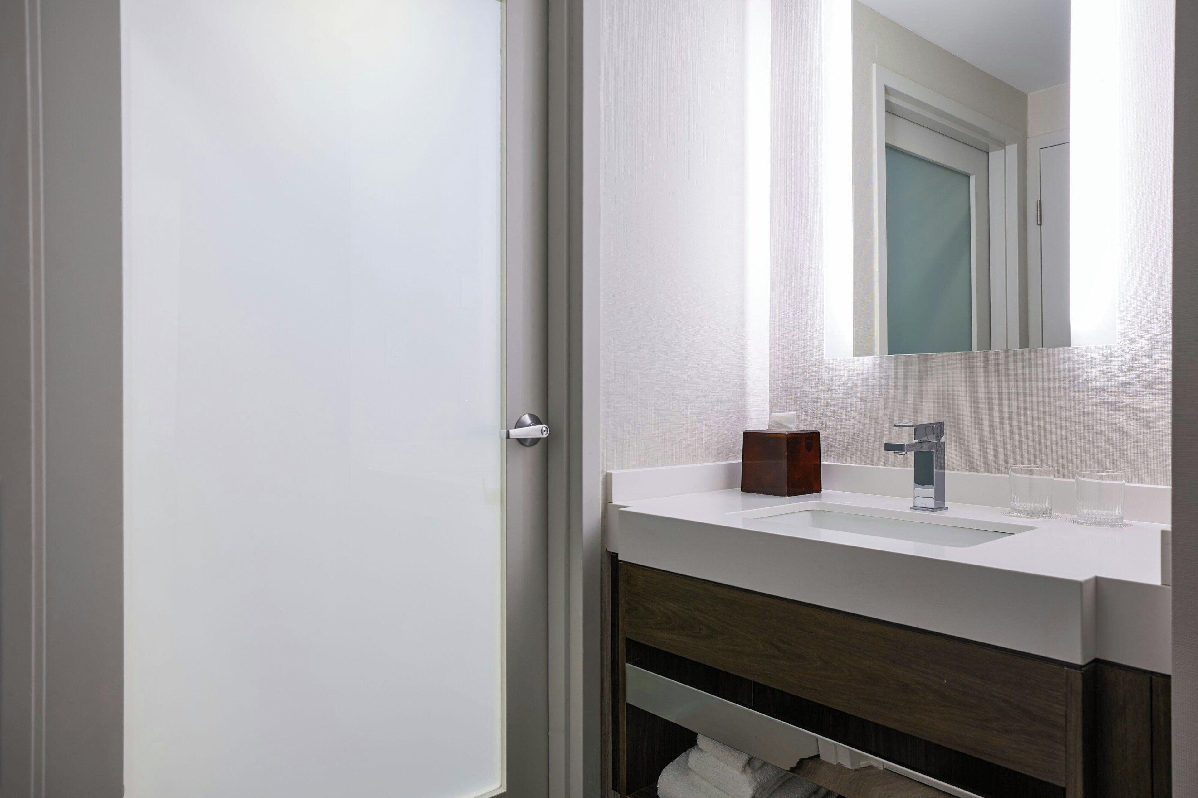 A modern bathroom with a white sink, a mirror, and a wooden vanity.
