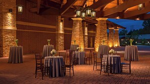 An outdoor dining area with brick walls and stone pillars, tables with grey tablecloths, and chairs.