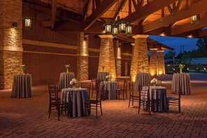 An outdoor dining area with brick walls and stone pillars, tables with grey tablecloths, and chairs.