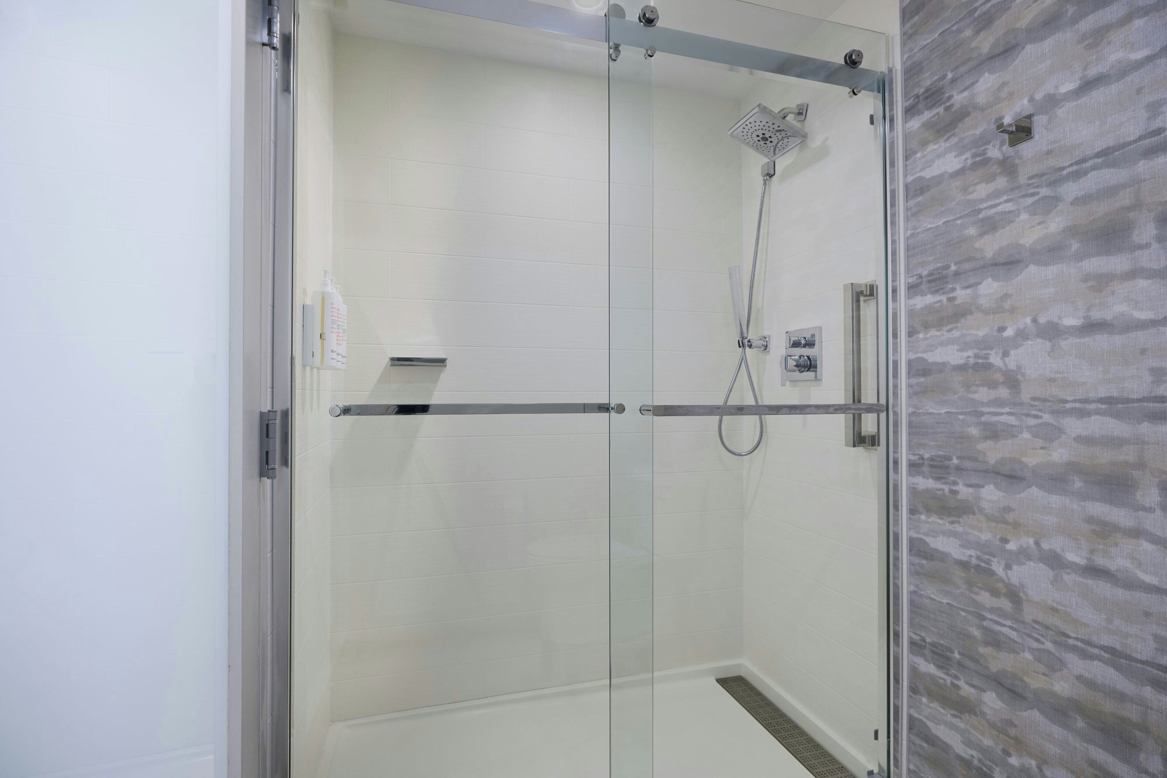 A glass-enclosed shower with a handheld showerhead and a wall-mounted control panel.