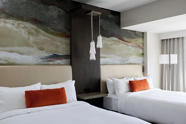 Habitación de hotel con dos camas, un cuadro abstracto grande en la pared y una lámpara colgante moderna.