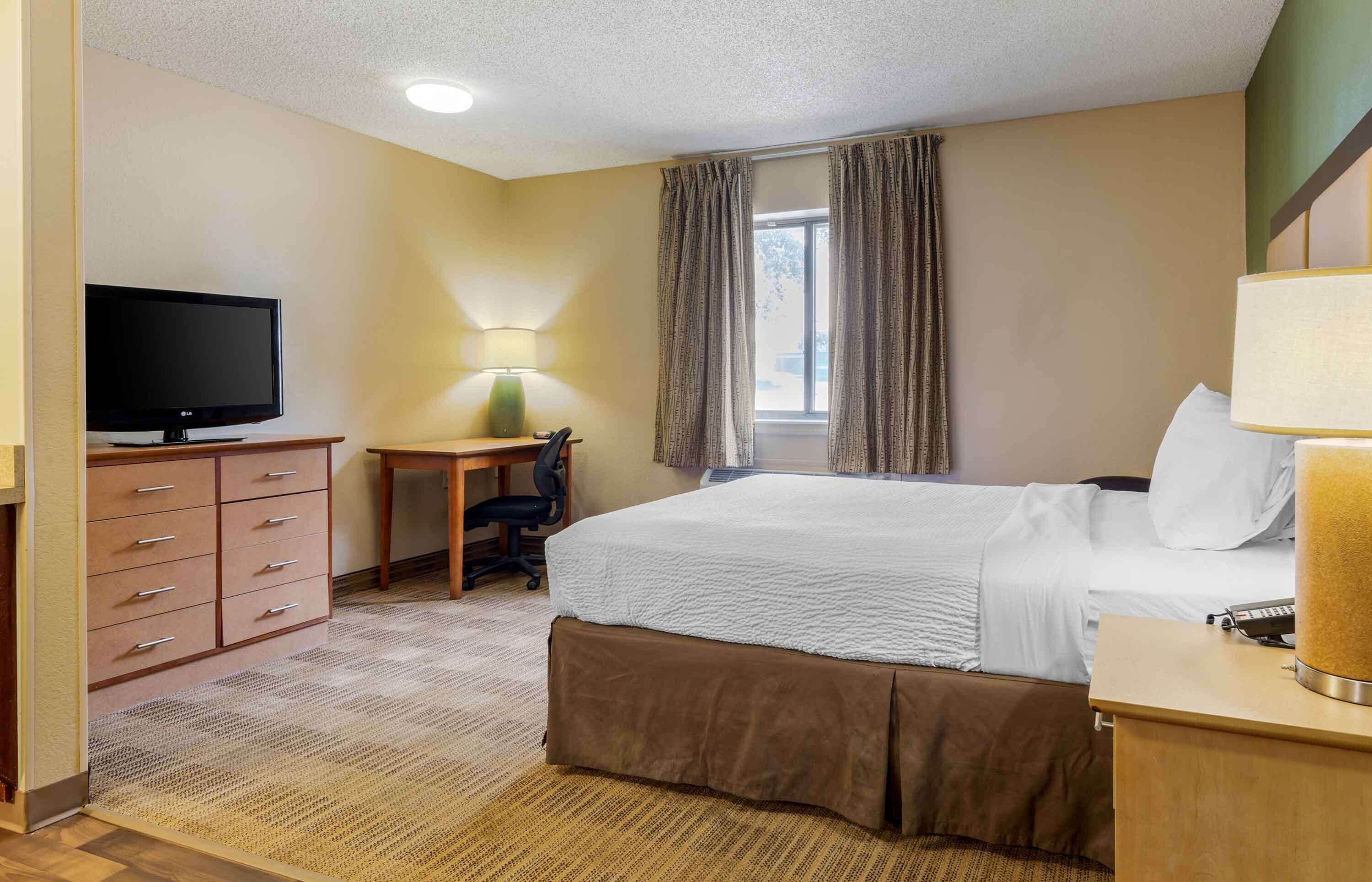 A hotel room with a bed, a desk with a chair, a television, and a lamp.