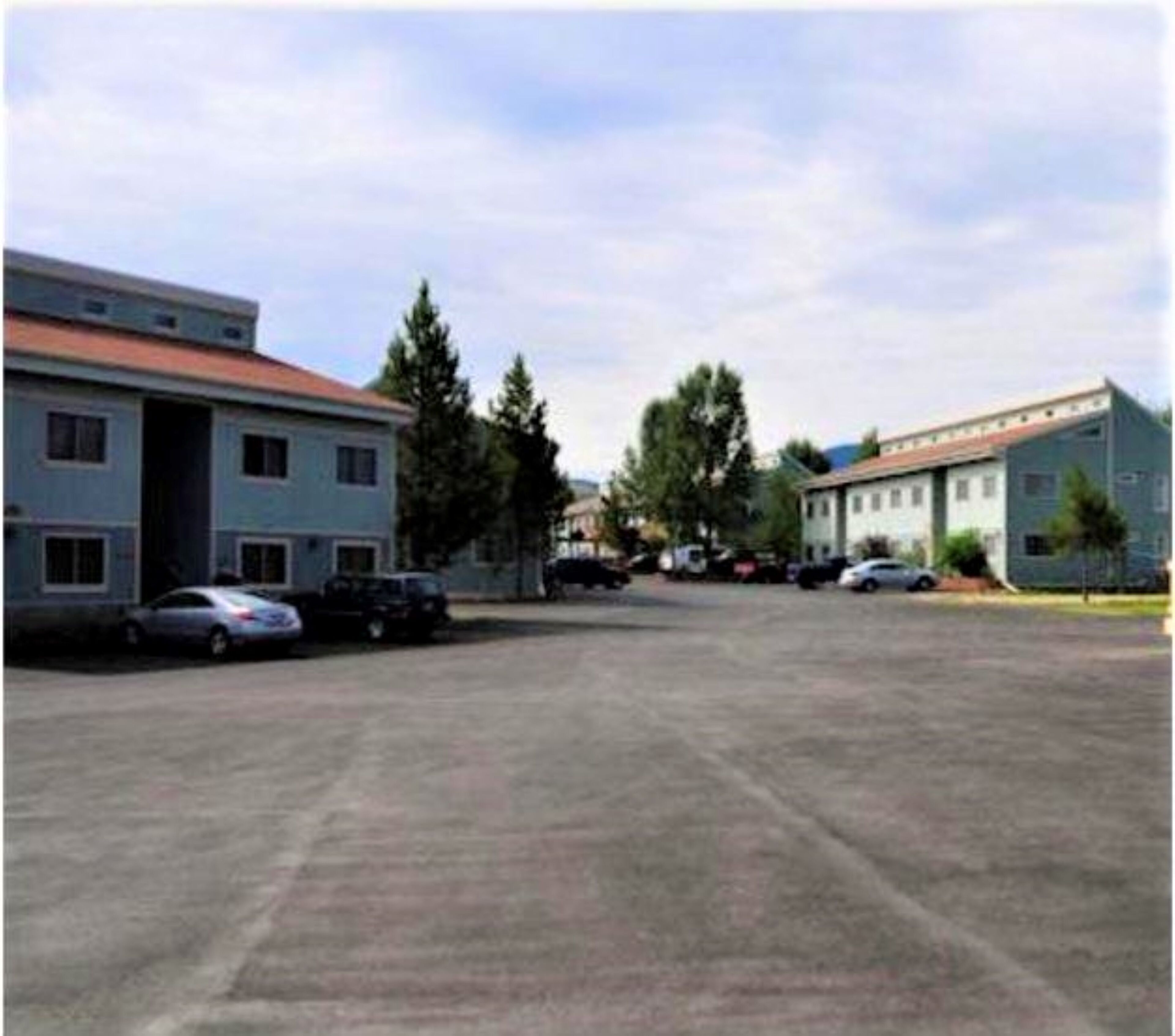 A parking lot with several cars and two buildings with flat roofs.