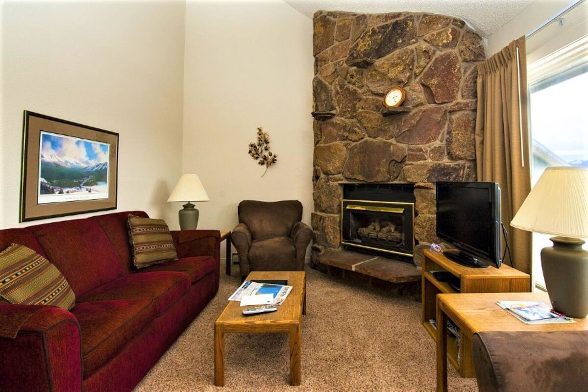 A cozy living room with a stone fireplace, a television, a red sofa, and a coffee table.