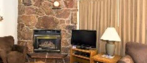 Una sala de estar con chimenea de piedra, un televisor y dos sillones.