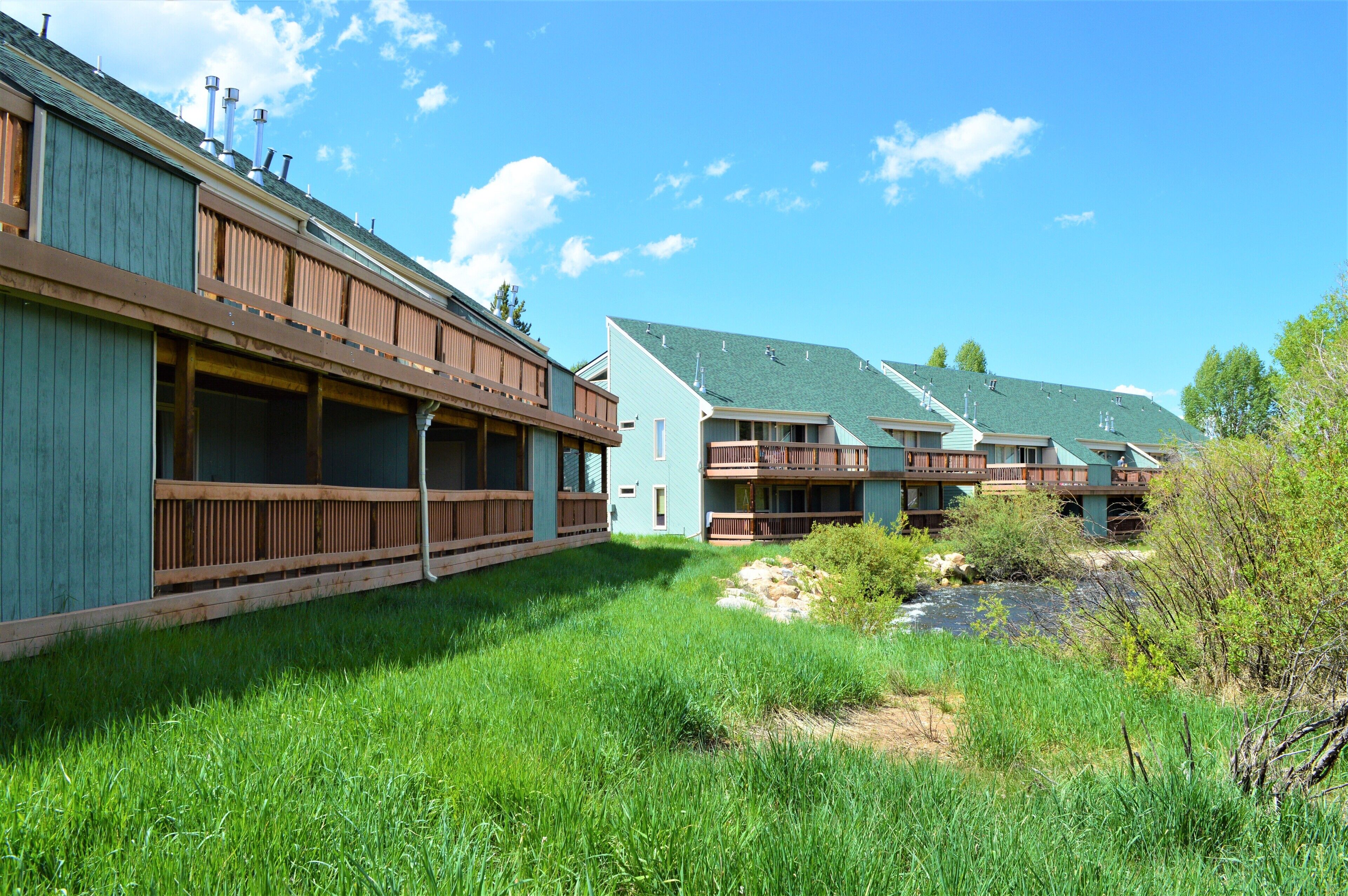 Une rangée de cabanes dotées de balcons en bois, une zone herbeuse et un petit ruisseau.
