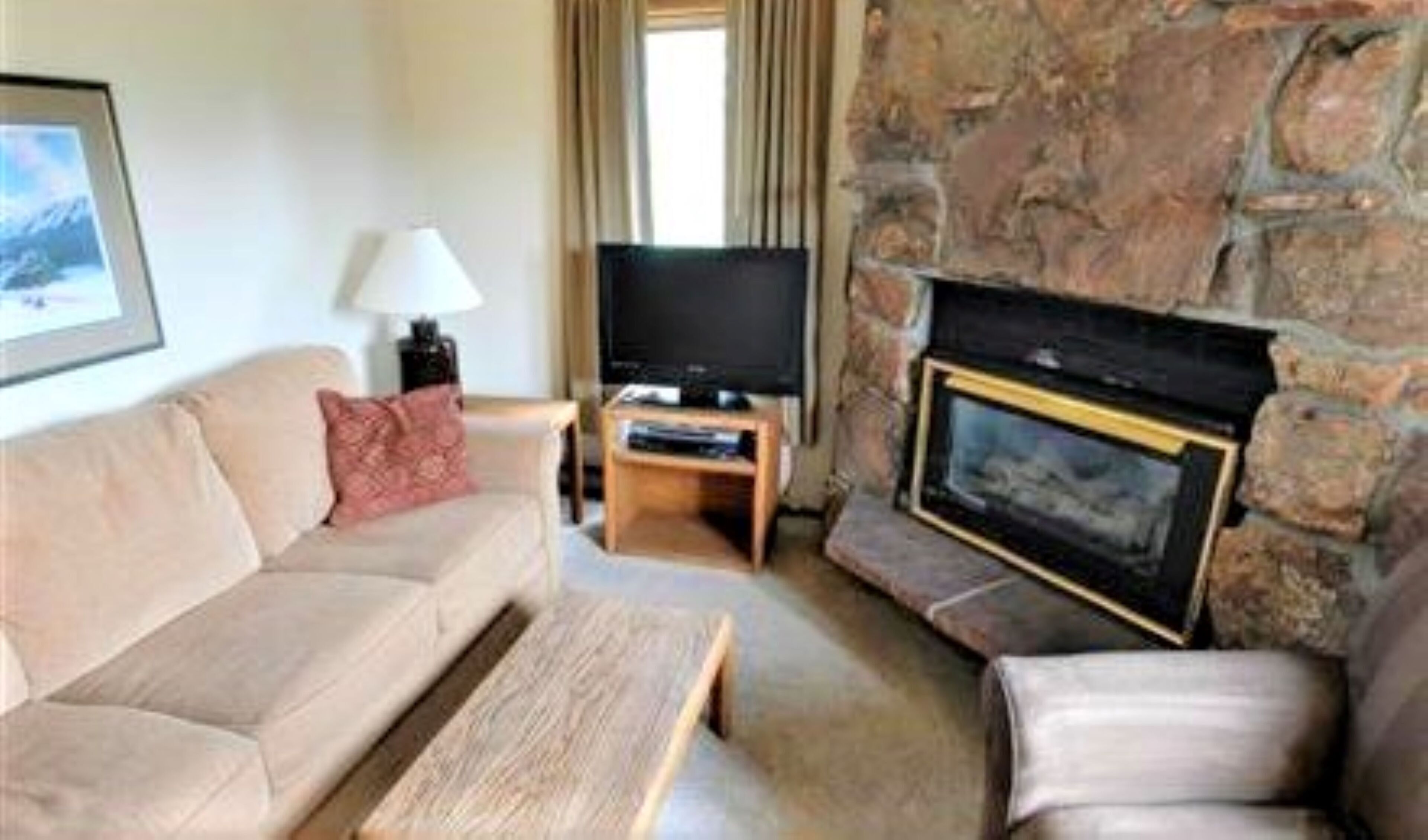 A living room with a stone fireplace, a sofa, a coffee table, and a television on a stand.