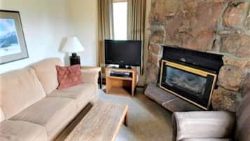 A living room with a stone fireplace, a sofa, a coffee table, and a television on a stand.