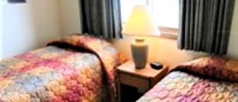 Habitación de hotel con dos camas, una mesita de noche con lámpara y una ventana con cortinas.
