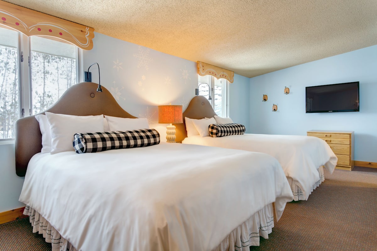 A hotel room with two beds, a TV, a dresser, and a window with a view of trees.