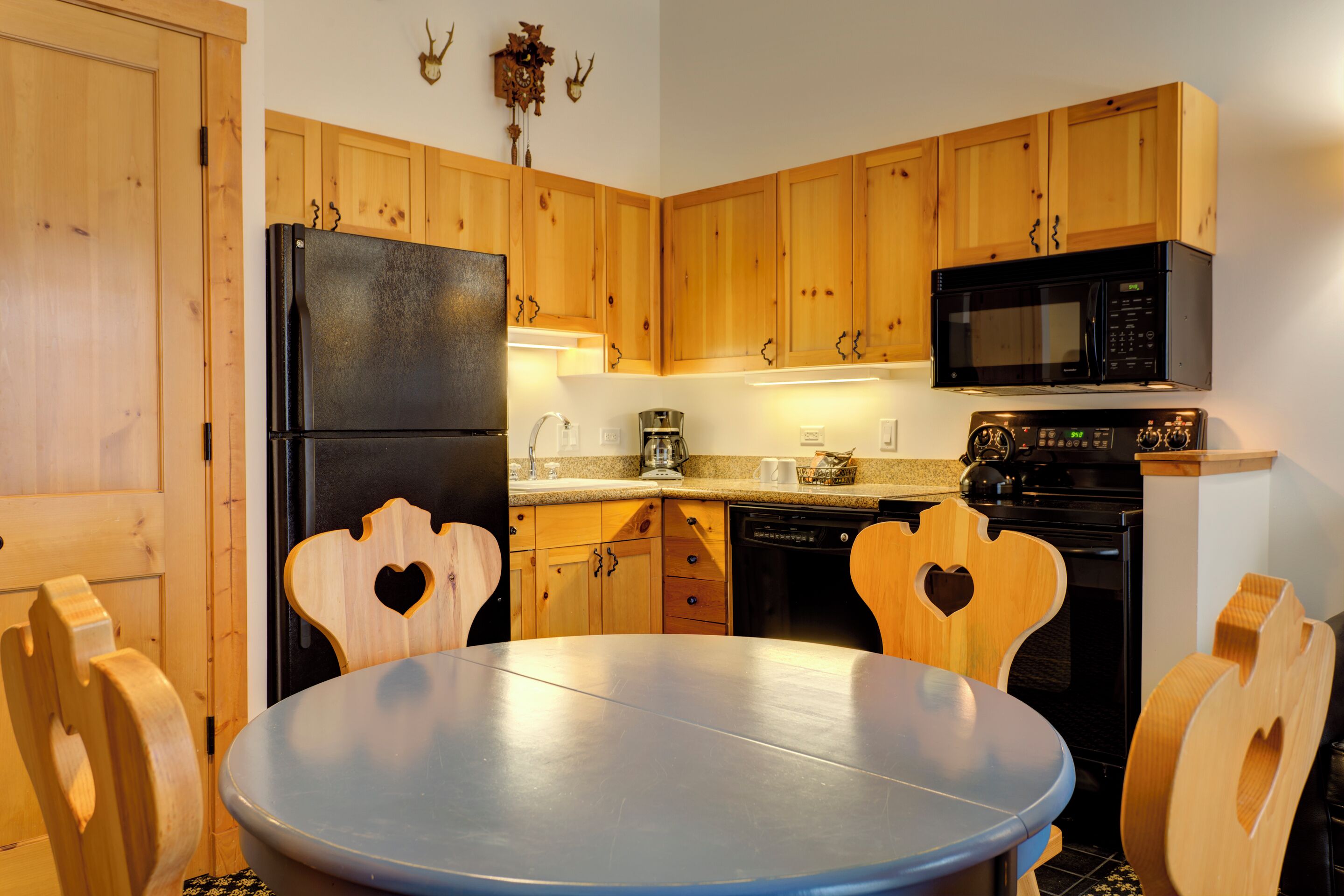 A kitchen with wooden cabinets, a black refrigerator, a microwave, a stove, and a table with heart-shaped chairs.