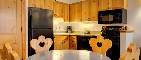 A kitchen with wooden cabinets, a black refrigerator, a microwave, a stove, and a table with heart-shaped chairs.