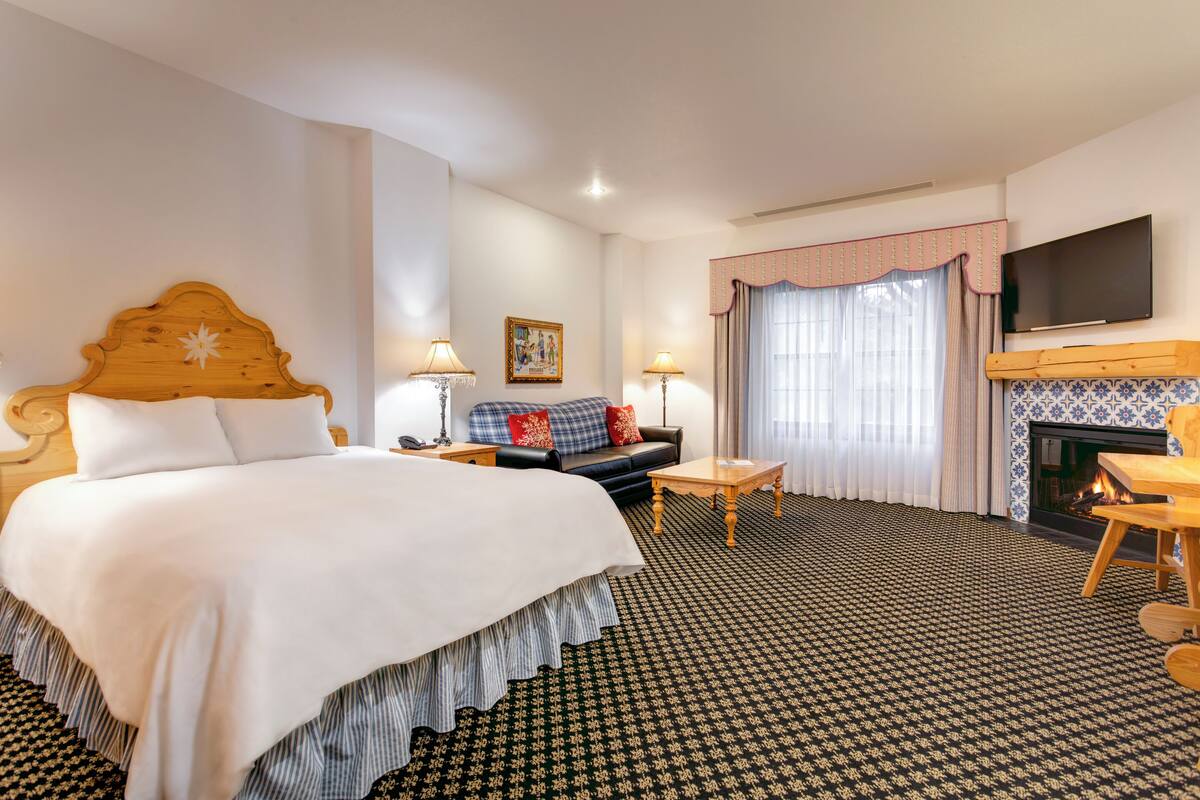A hotel room with a large bed, a sofa, a small table, a fireplace, and a television.
