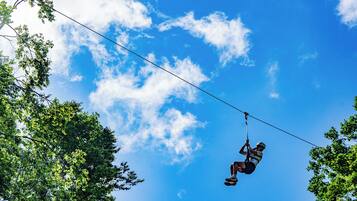 Eine Person saust an einem Zipline durch einen strahlend blauen Himmel, flankiert von Bäumen.