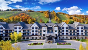 Un grand hôtel à étages, doté d’une cour intérieure et offrant une vue sur un paysage vallonné aux couleurs automnales.