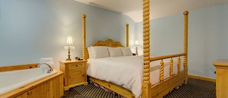 Una cama con dosel, un cabecero de madera, una mesita de noche con lámpara, un banco de madera y una bañera.