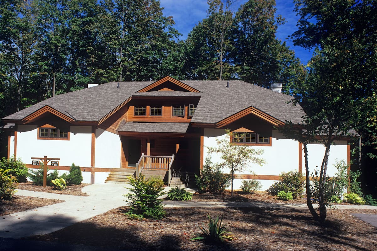 A two-story log cabin with a front porch, surrounded by trees.