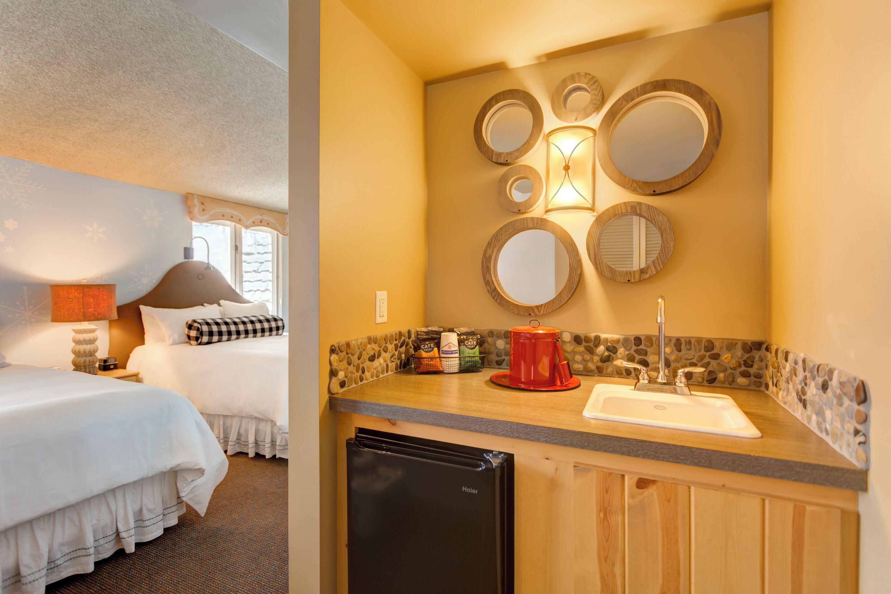 A hotel room with two beds, a kitchenette, and a wall-mounted mirror.