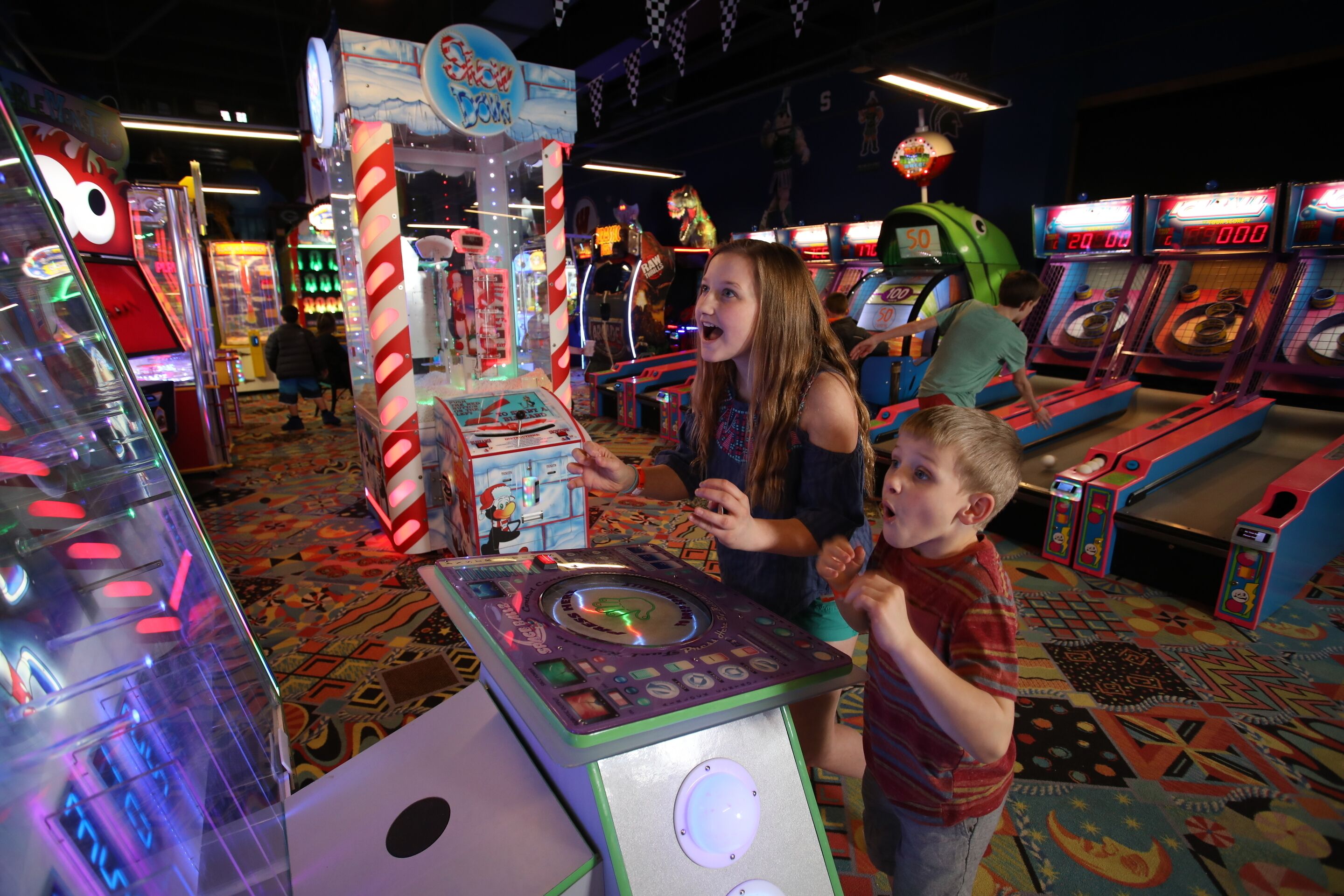 A room with arcade machines, a large candy cane decoration, and a patterned carpet.