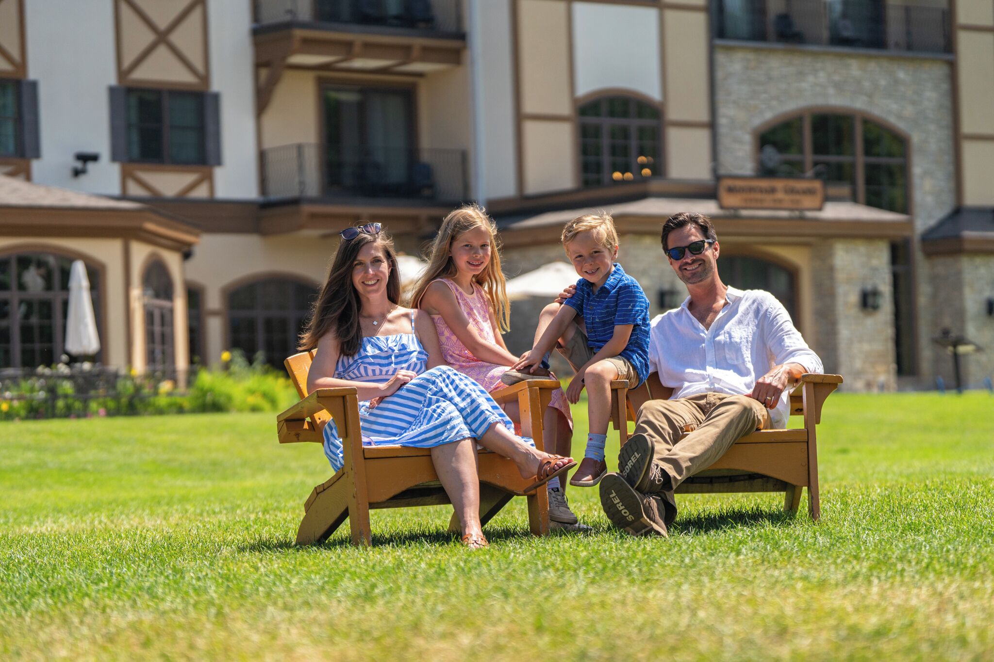 A family sitting on a bench in front of a building with a stone facade and arched windows.