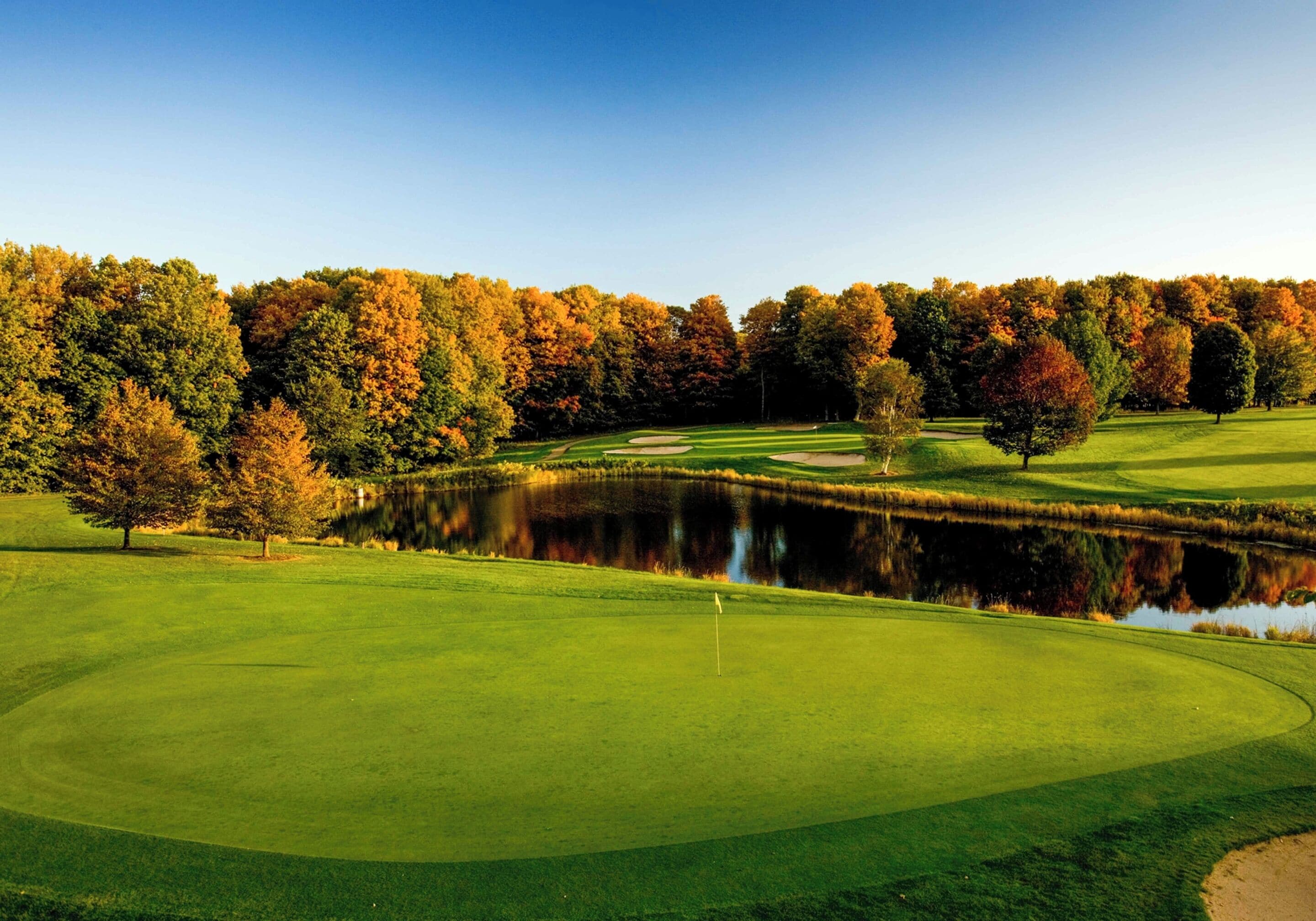 A golf course with a pond, trees, and a clear sky.