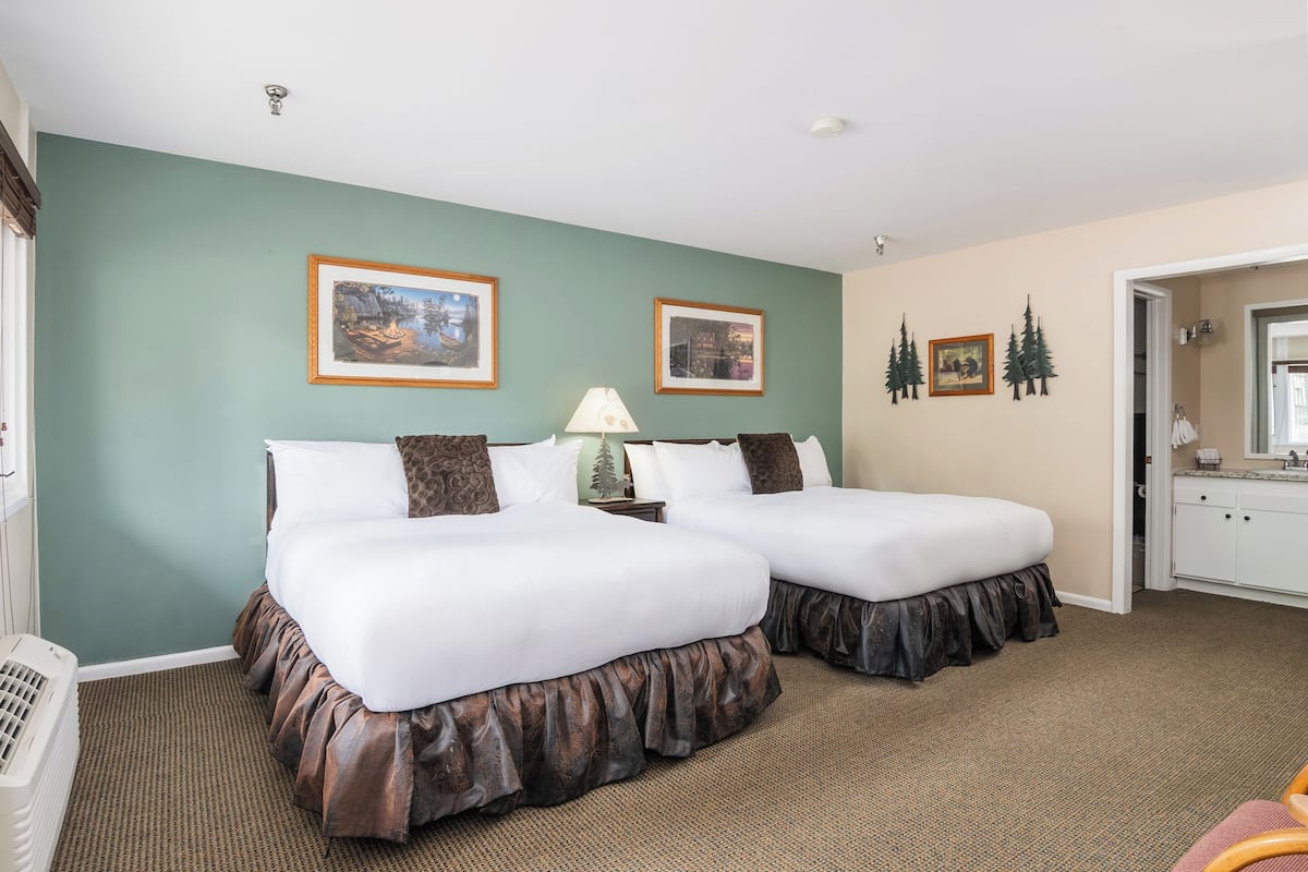 A hotel room with two beds, a nightstand, a lamp, and framed pictures on the wall.