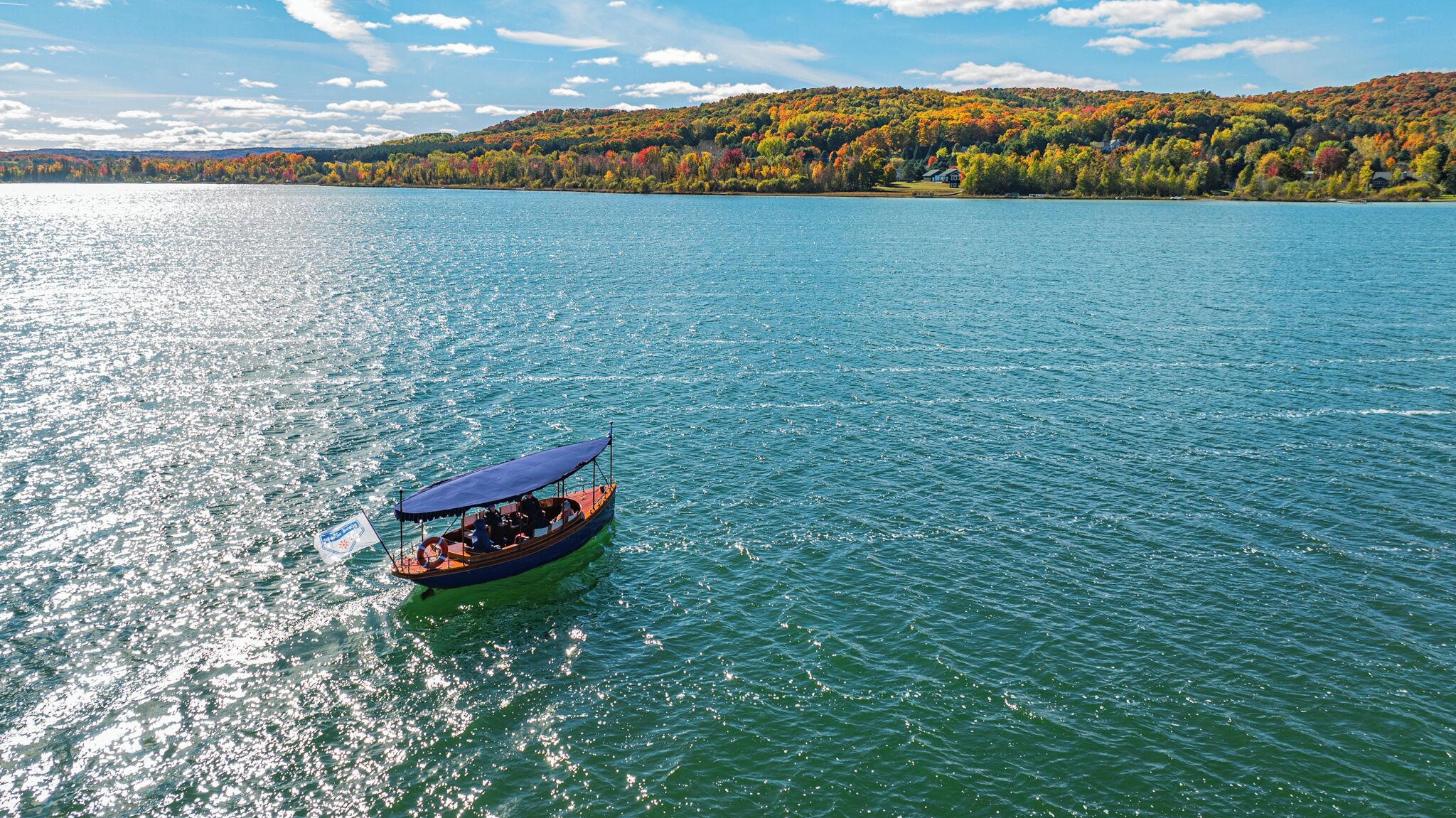 A boat on a calm lake with a forested hillside in the background.