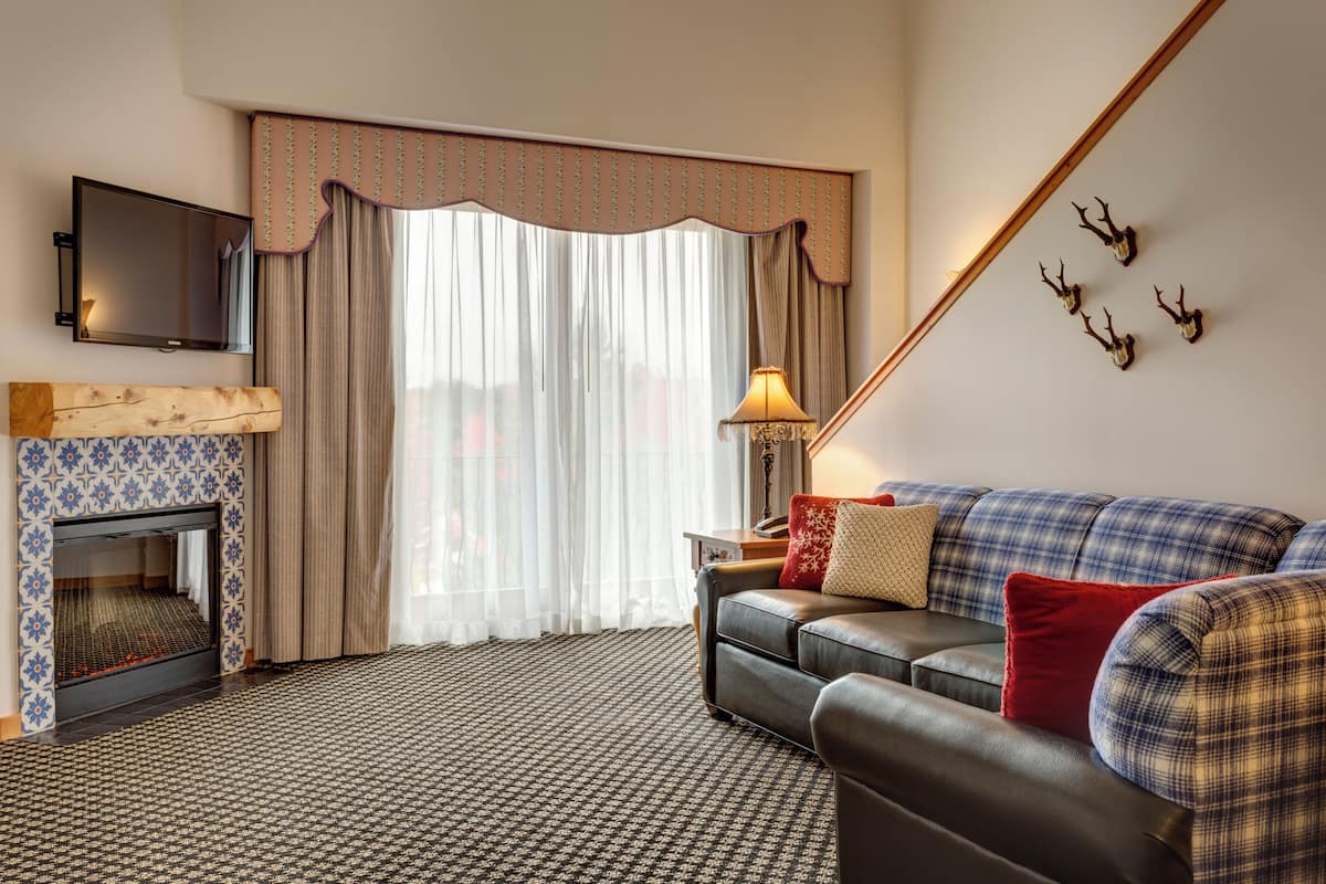 A room with a fireplace, a sofa, a television, and a large window with curtains.