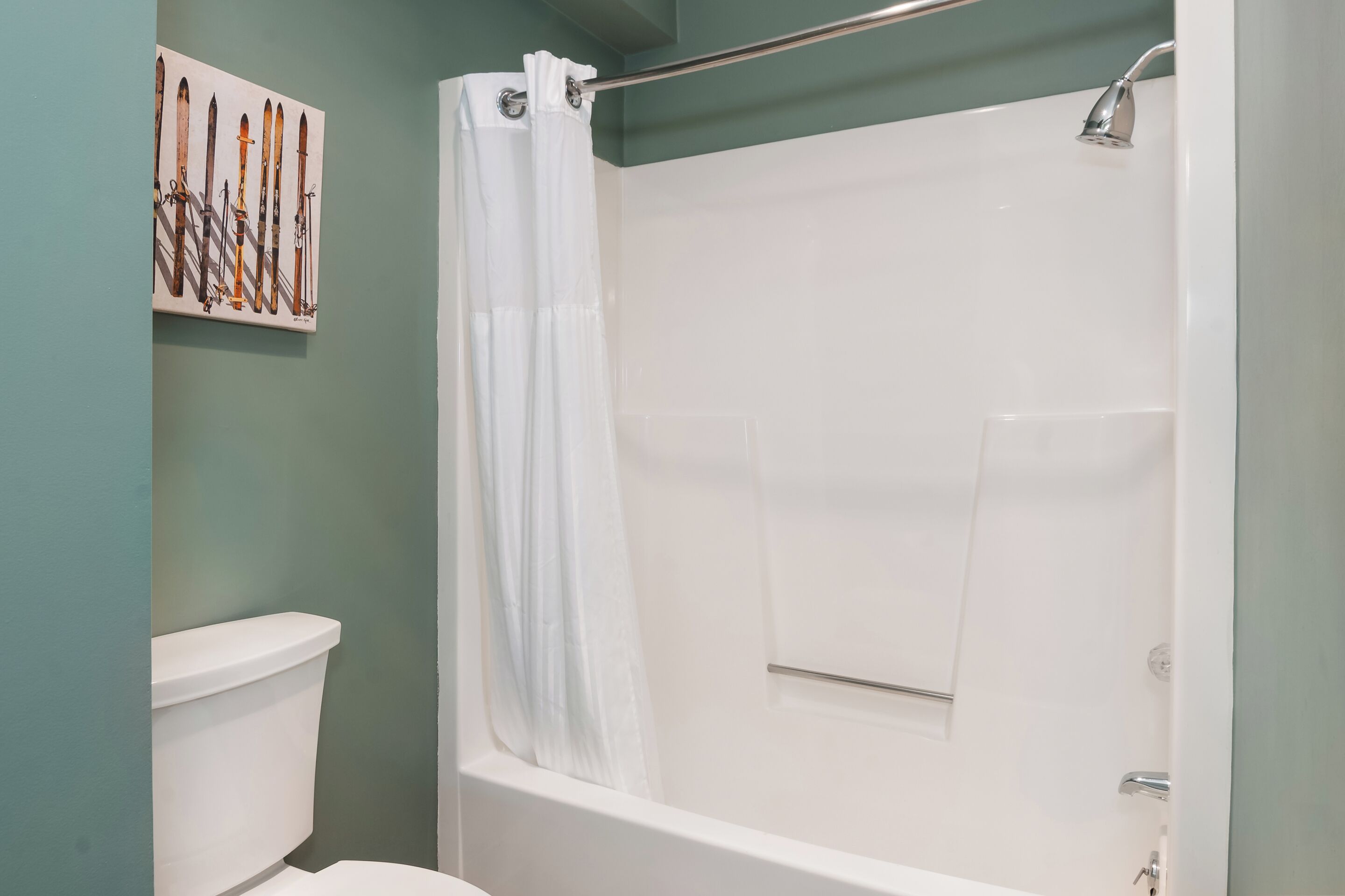 Une salle de bain avec douche, toilettes et un porte-skis fixé au mur.