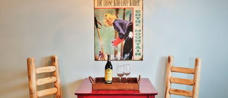 A table with a bottle and glasses, two wooden chairs, and a poster on the wall.