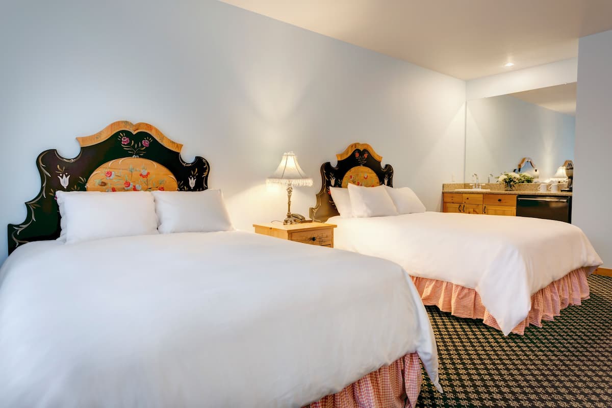 Two beds with ornate wooden headboards, a bedside table with a lamp, a dresser, and a mirror.