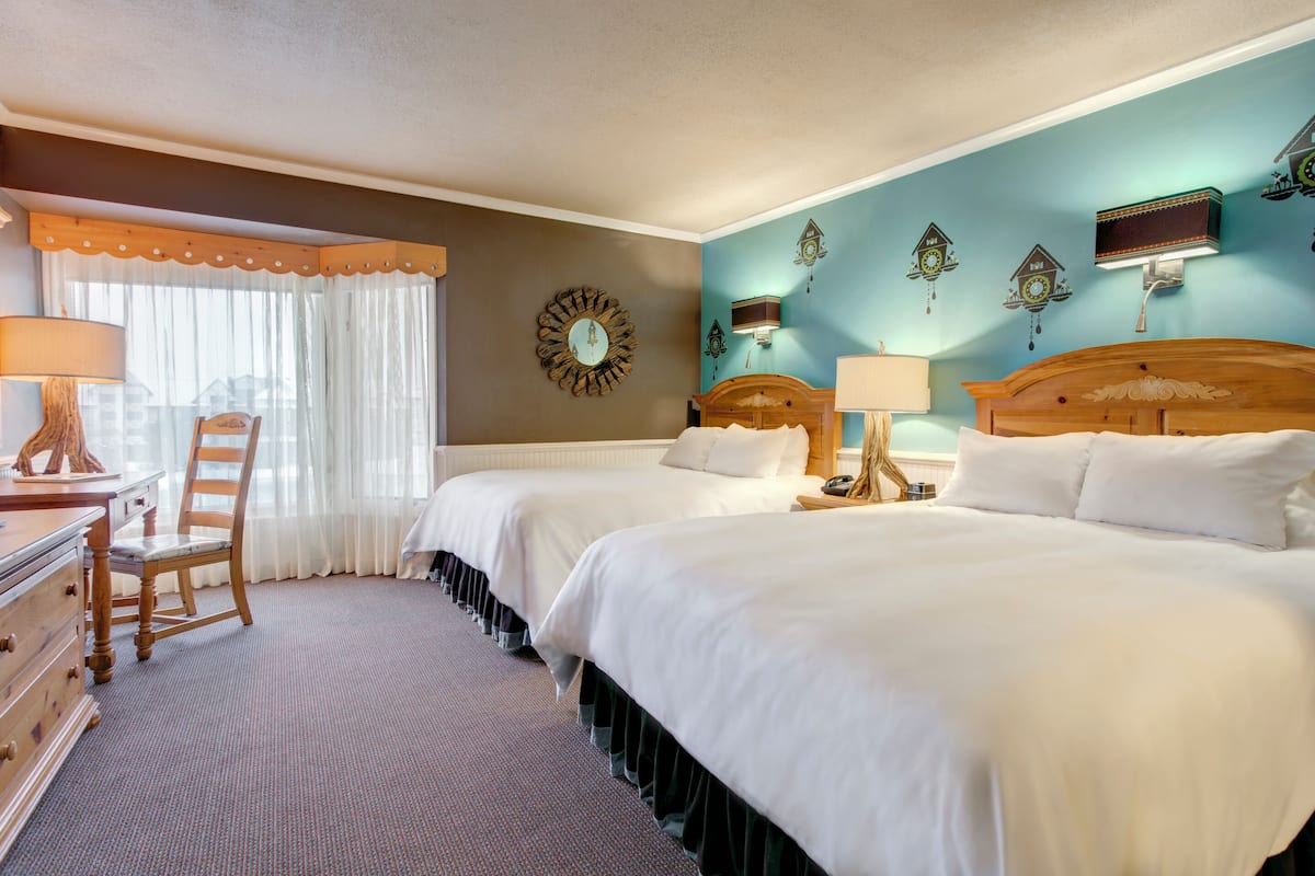 A hotel room with two beds, a desk, a chair, and a large window with curtains.