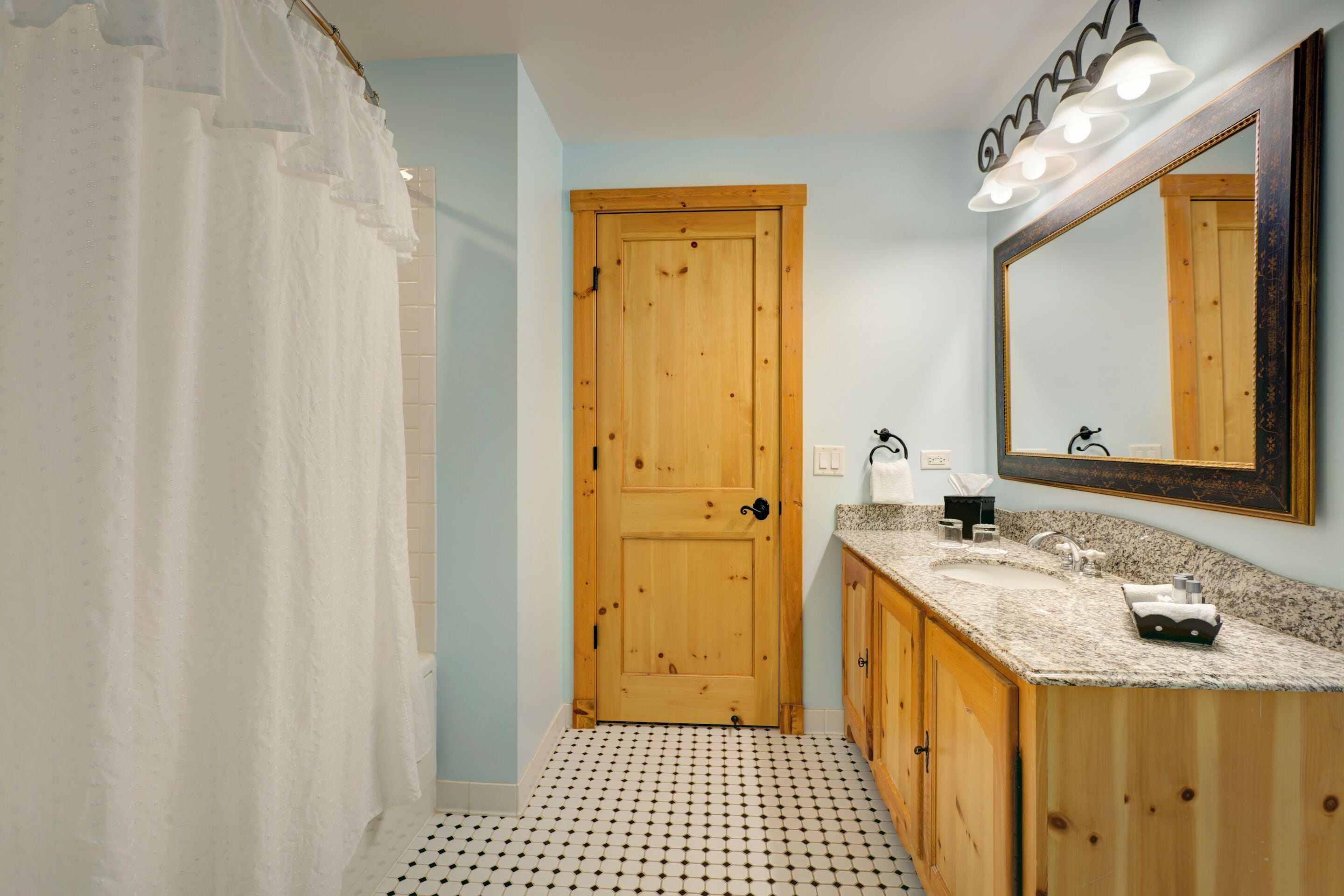 A bathroom with a wooden door, a sink with a mirror, and a patterned floor.