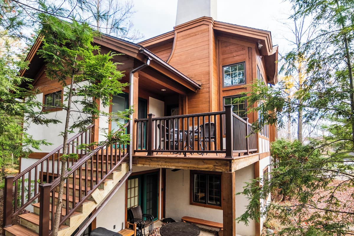 A multi-level wooden house with a balcony, stairs, and outdoor seating.