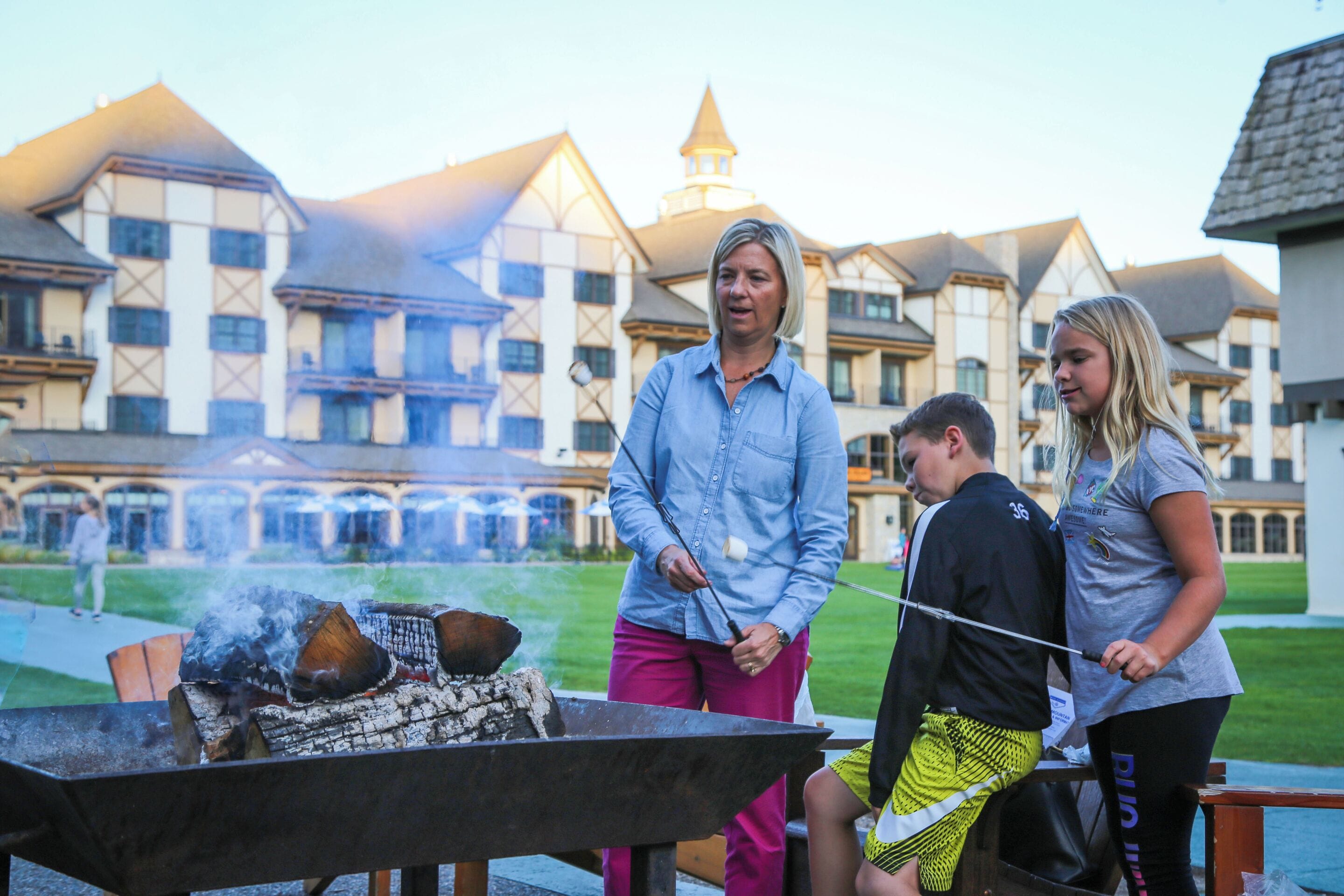 A group of people around a barbecue grill with a large building in the background.