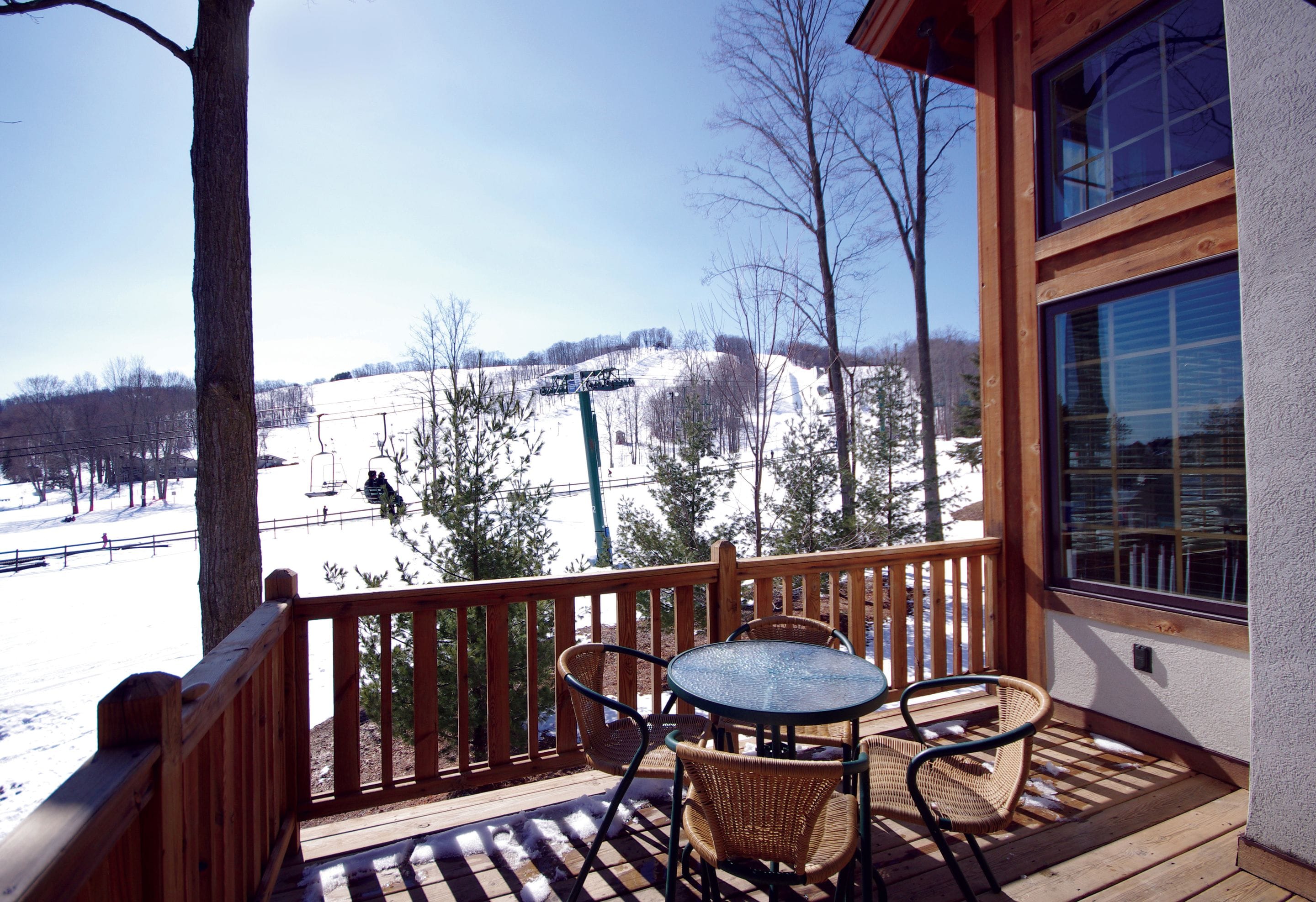 A wooden deck with a table and chairs, overlooking a snowy landscape with a ski lift in the distance.