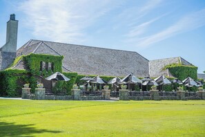 A building with a tiled roof, ivy-covered walls, outdoor seating with umbrellas, and a well-maintained lawn.