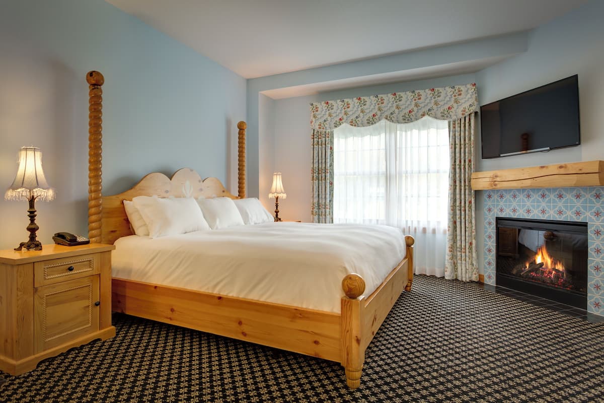 A bedroom with a wooden bed, bedside lamps, a fireplace, and a TV mounted on the wall.