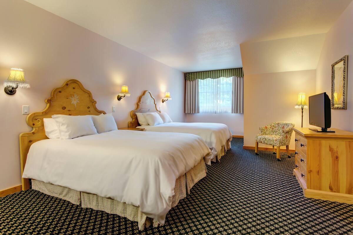 A hotel room with two beds, a wooden dresser, a television, and a window with curtains.