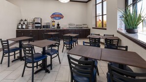 Un coin petit-déjeuner avec des tables et des chaises, un espace dédié au café et une grande fenêtre agrémentée d’une plante.